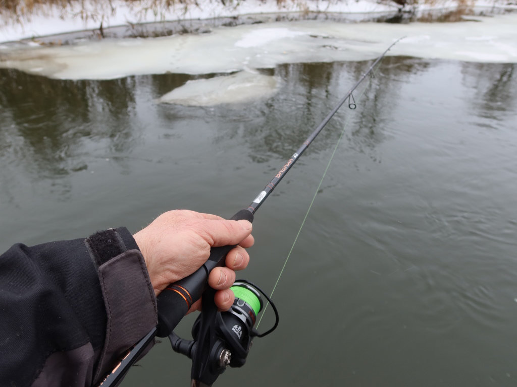 Спиннинг Lucky John Basara Спиннинг над открытой водой зимней реки с кусками льда на берегу. Вид от первого лица